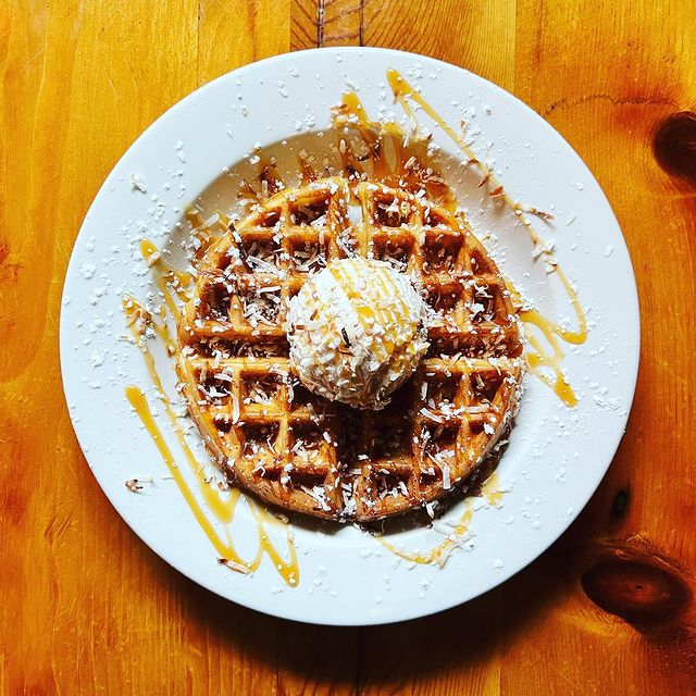 A waffle with ice cream and syrup on a wooden table.