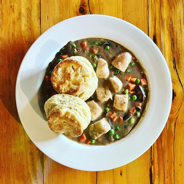 A bowl of stew with biscuits on a wooden table.